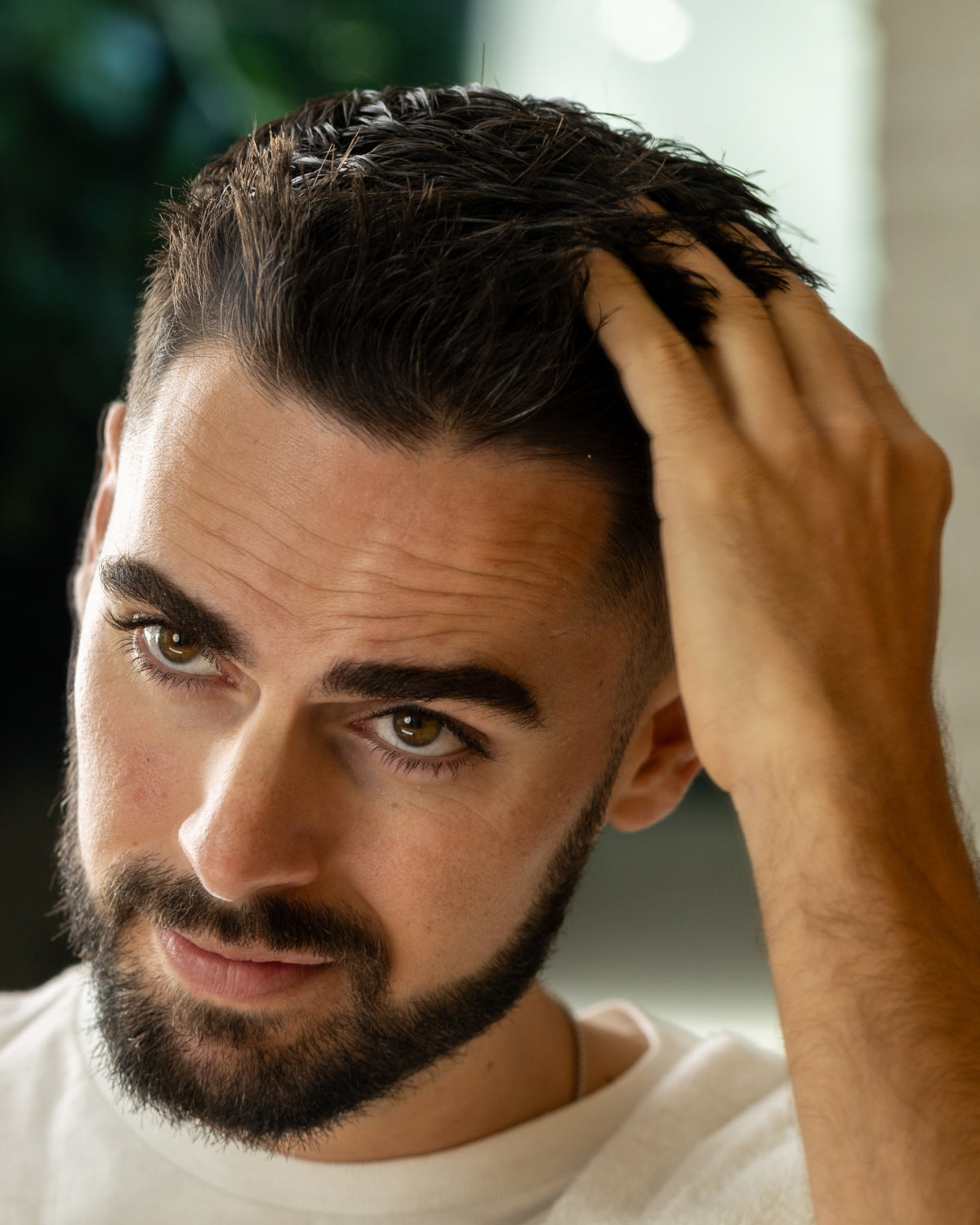 Man with a beard and styled hair adjusting his hair with a blurred background